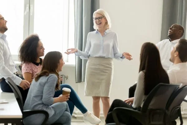 Smiling businesswoman leading a relaxed team discussion with diverse colleagues seated in a circle, symbolizing collaboration and open communication in a family business setting.