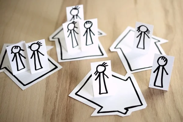 Paper cutouts of stick-figure families placed on drawn house shapes, symbolizing family structure, separation, or the concept of household boundaries